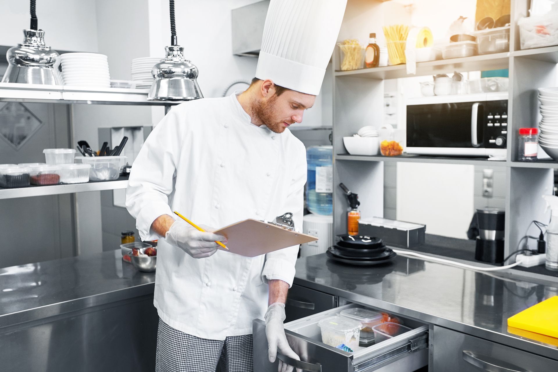 A chef is writing on a clipboard in a kitchen
