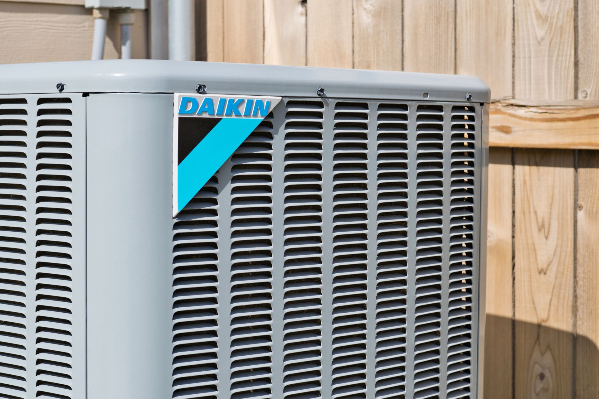 A daikin air conditioner is sitting next to a wooden fence.