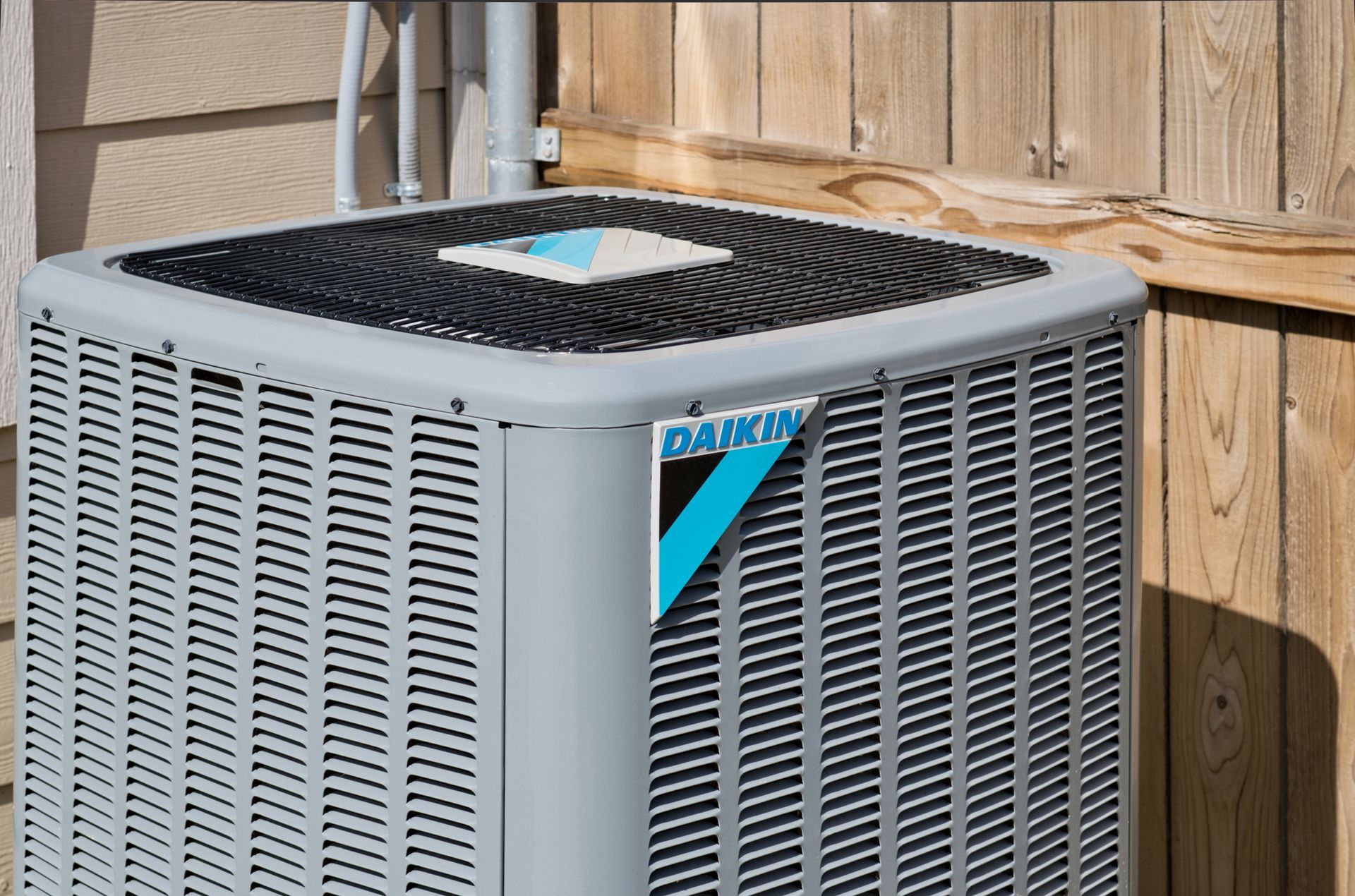 A daikin air conditioner is sitting next to a wooden fence.
