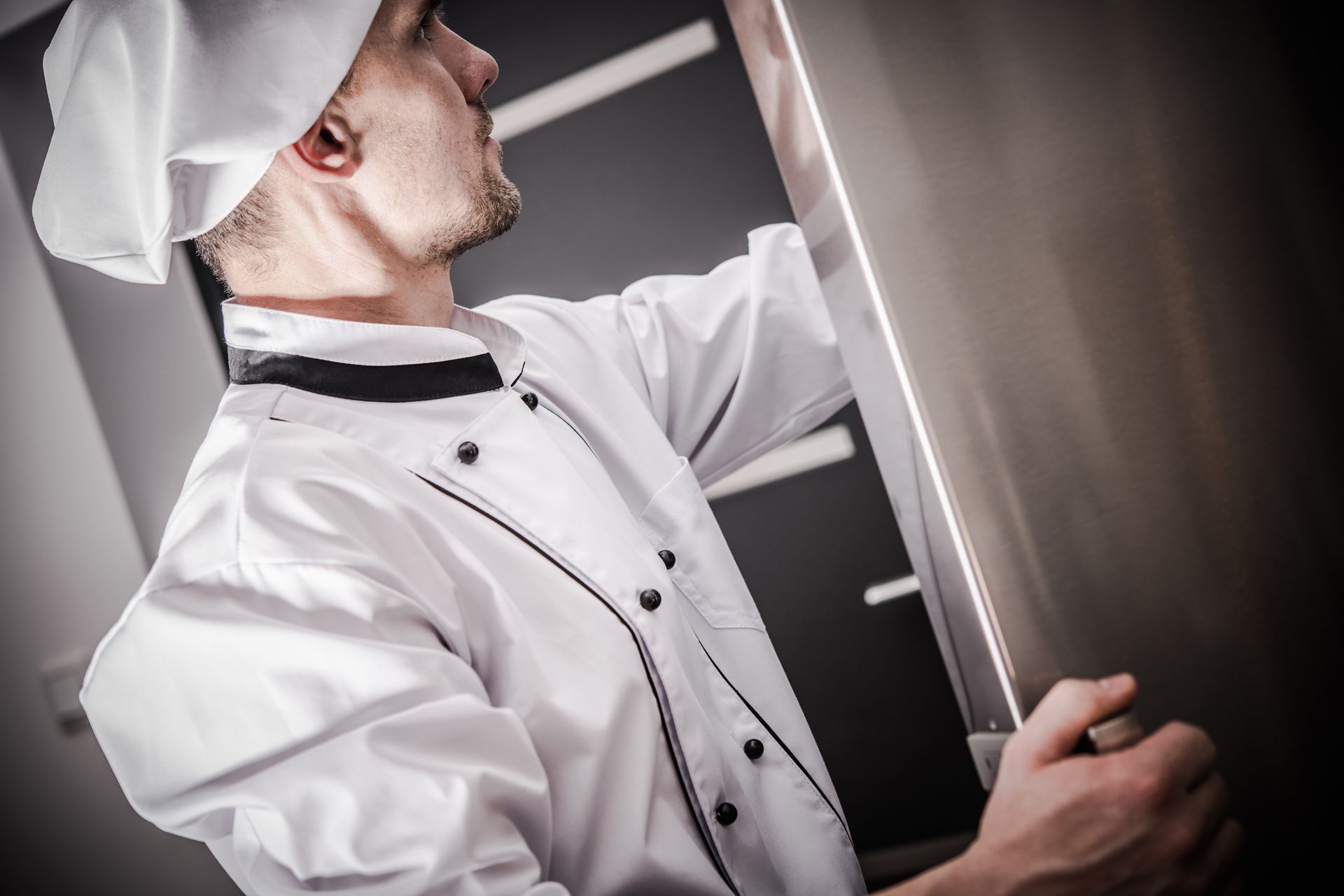 A chef is opening a refrigerator door in a kitchen