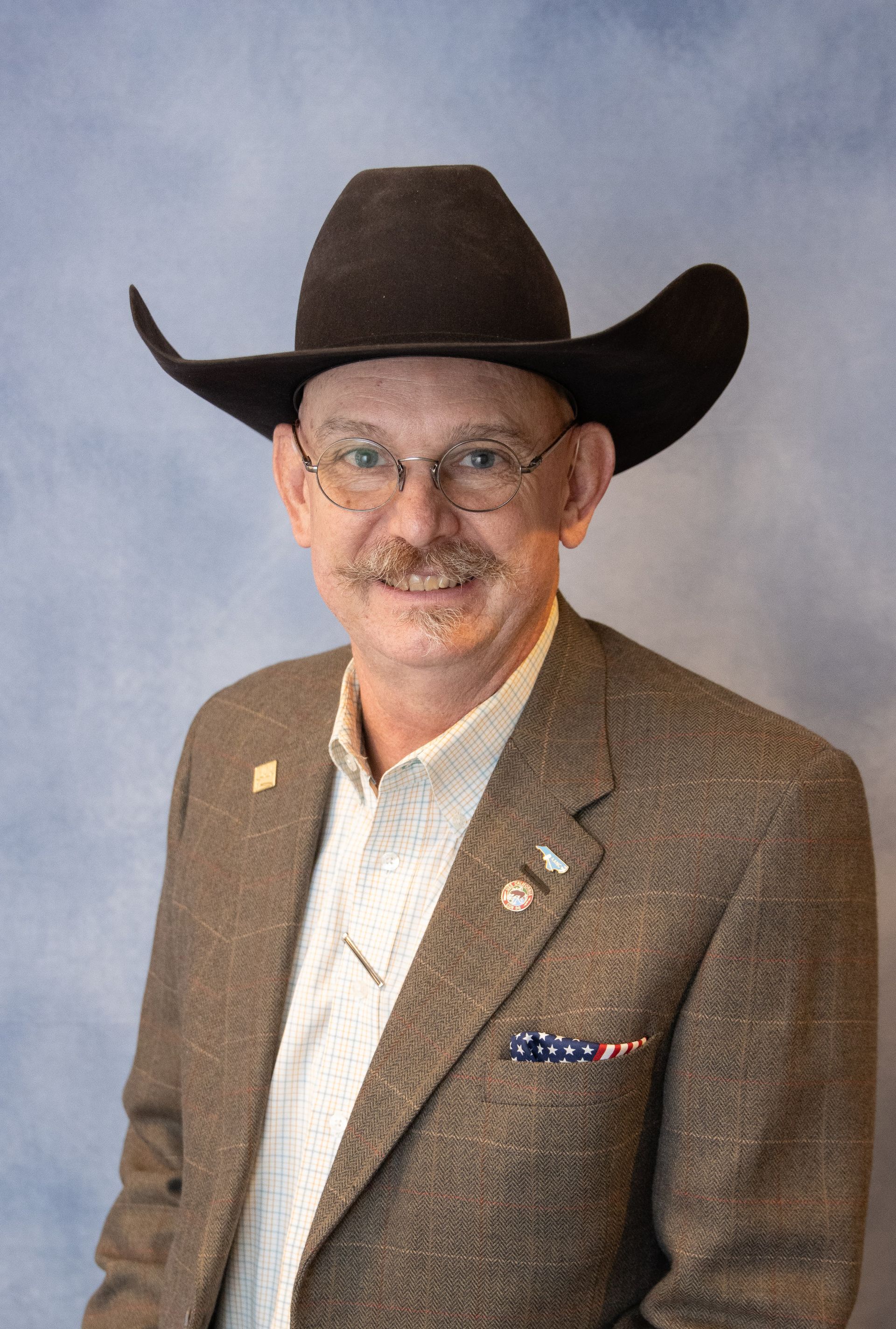 Man in cowboy hat and blazer smiles at the camera.
