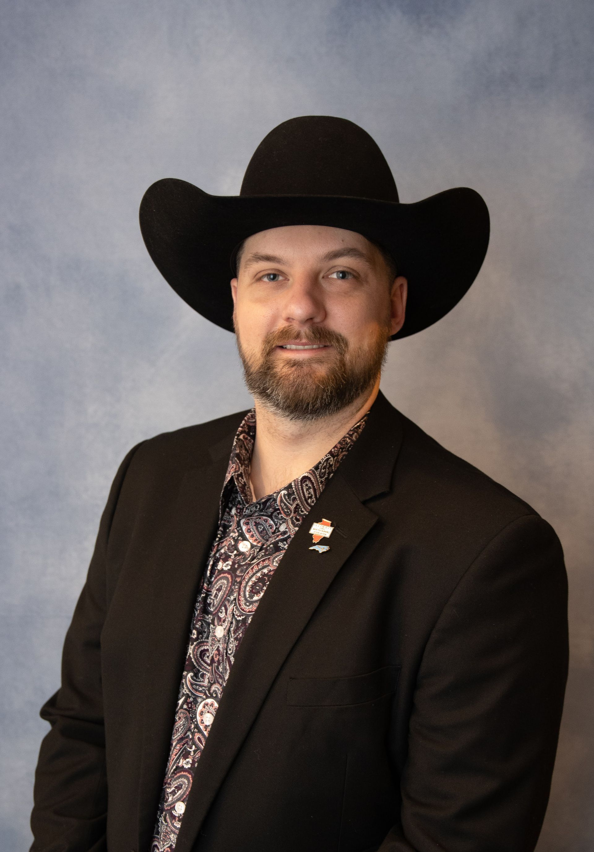 Man in cowboy hat and suit smiles against a blue backdrop.