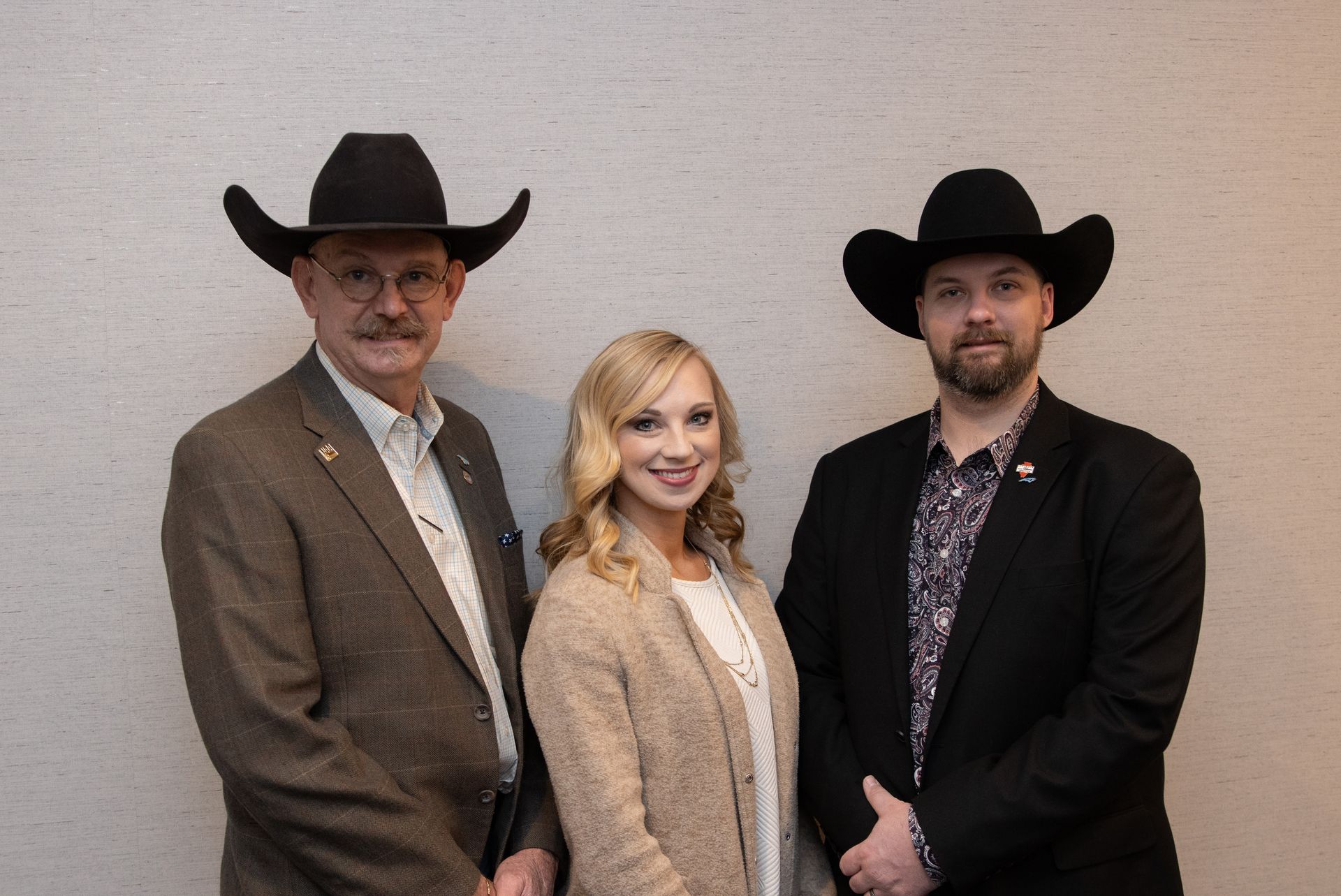 Three people wearing cowboy hats, posing in front of a neutral wall.