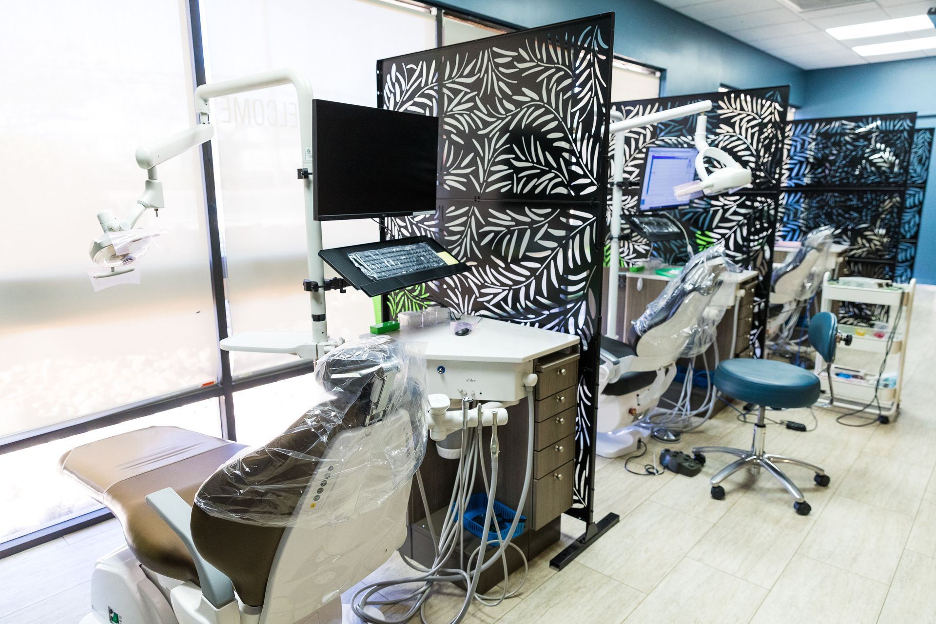 Dental office interior with patient chairs, equipment, and decorative privacy screens.