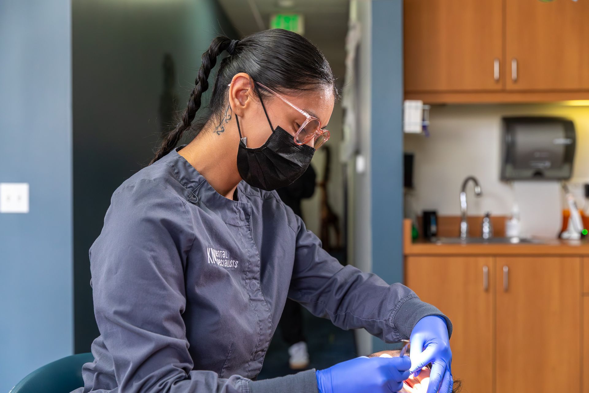 Dentist in scrubs and mask working on a patient's teeth in a dental office.