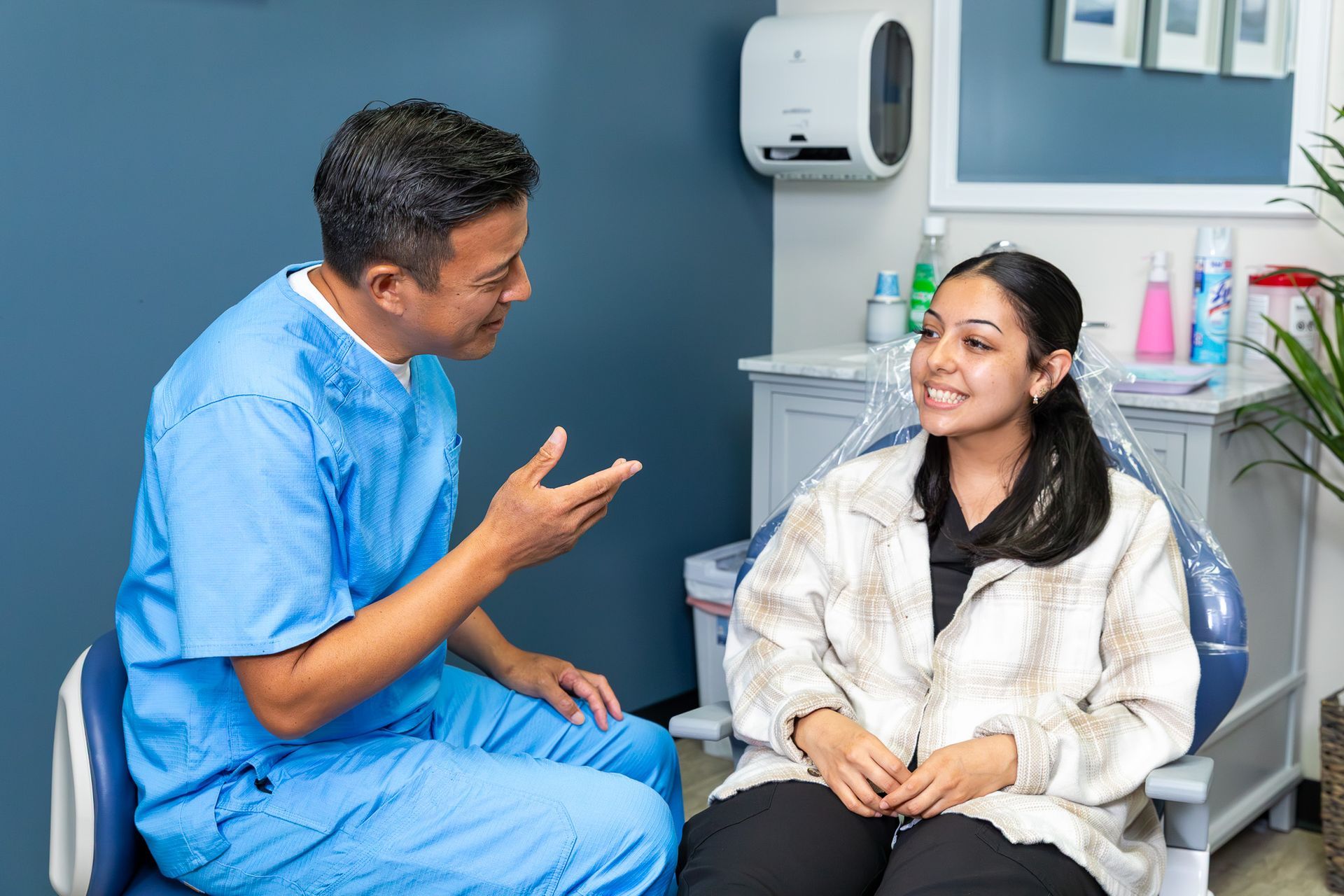 Dentist in scrubs talking to patient seated in a dental chair in a clinic.