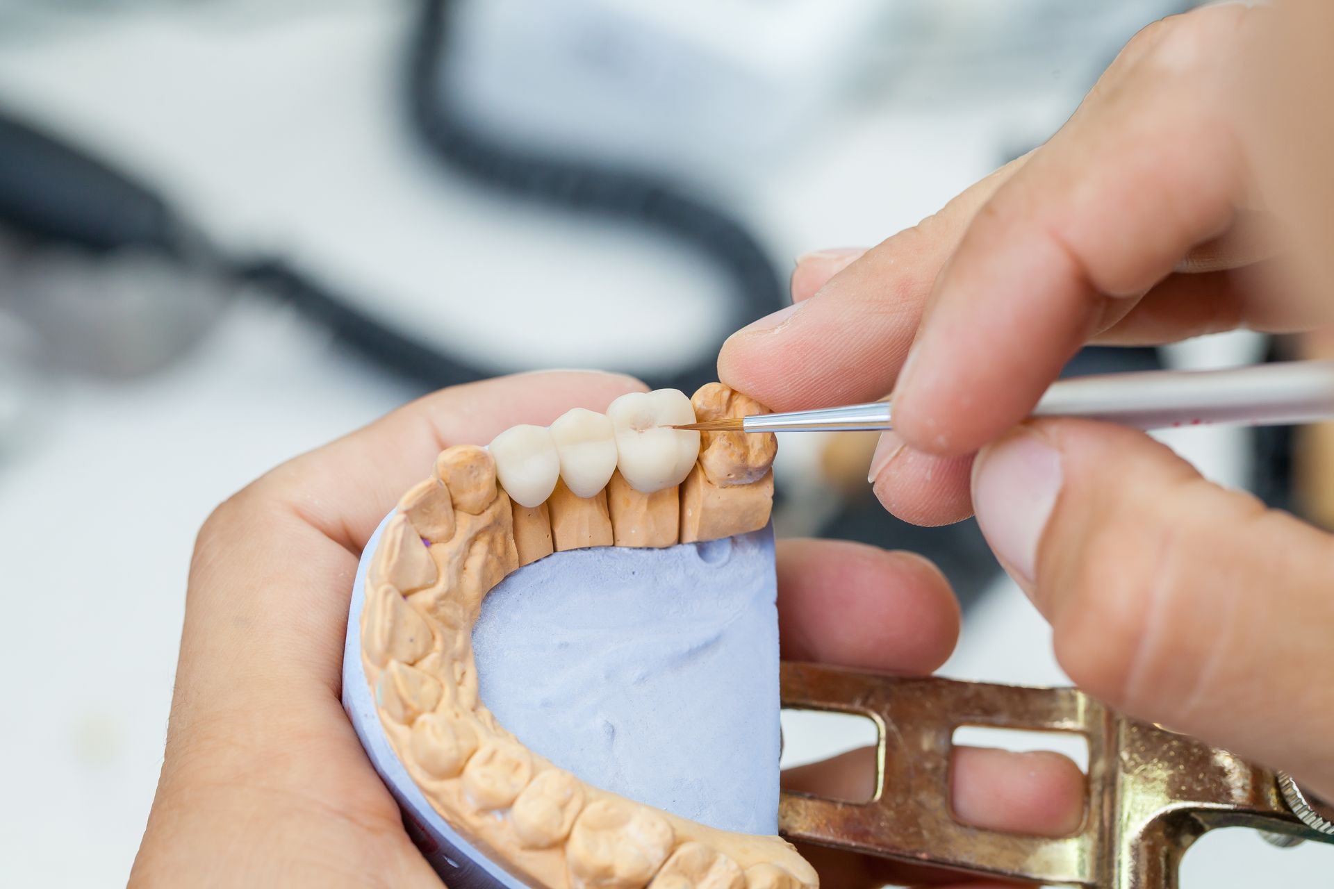 Dental technician using a tool to work on a model of teeth in a lab setting.