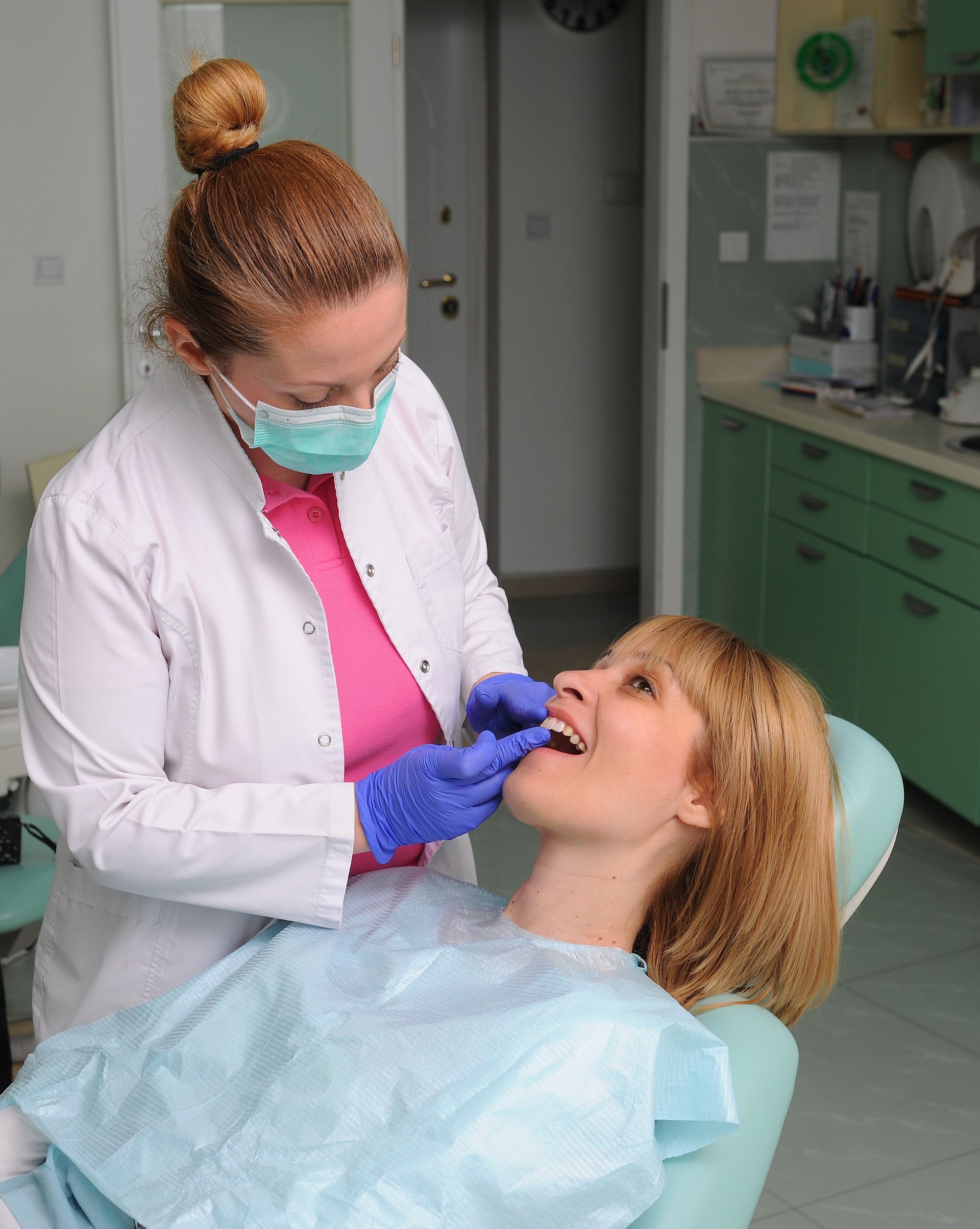 A woman is sitting in a dental chair while a dentist examines her teeth.