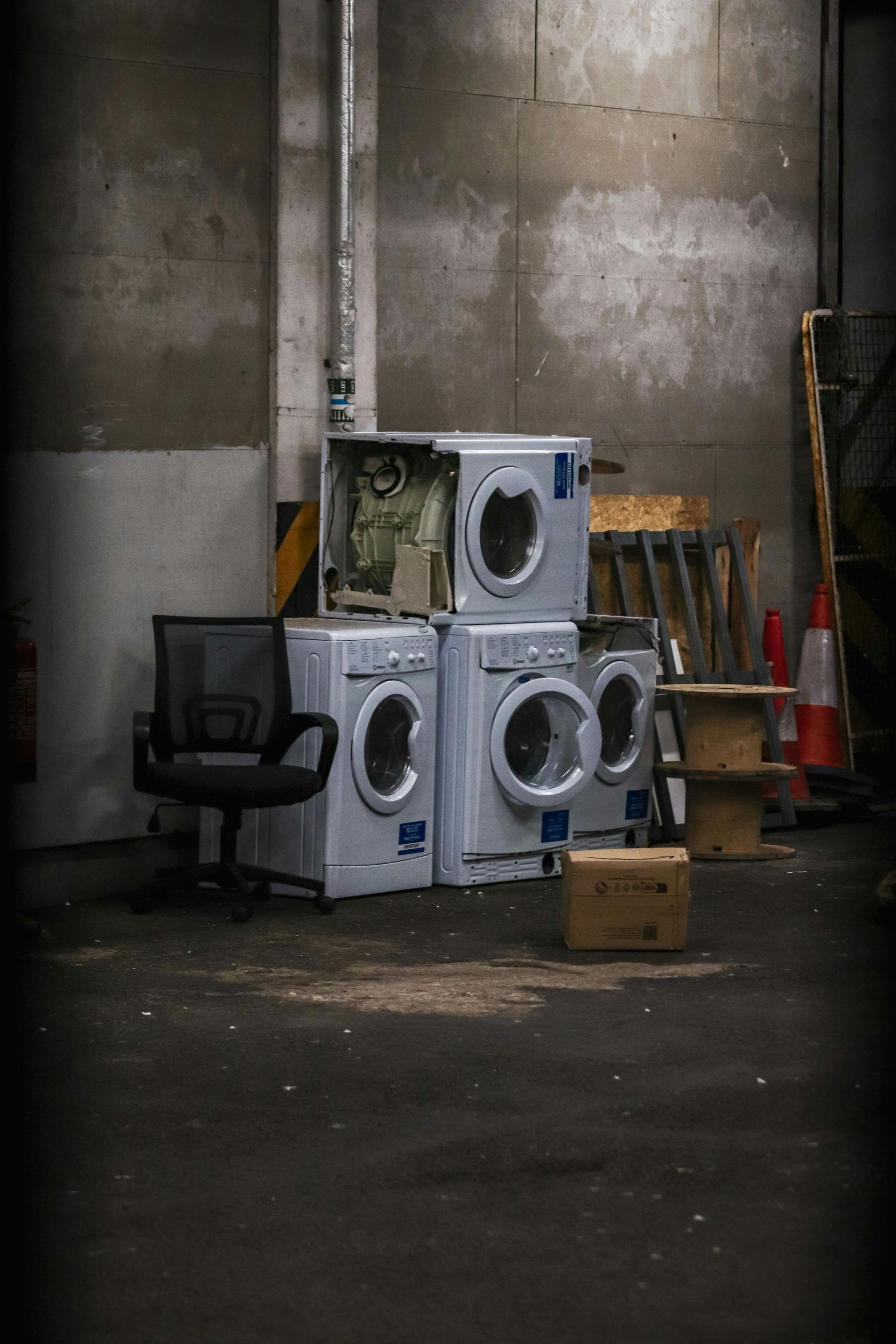 Stack of washing machines, office chair, boxes, and ladder inside a storage space.