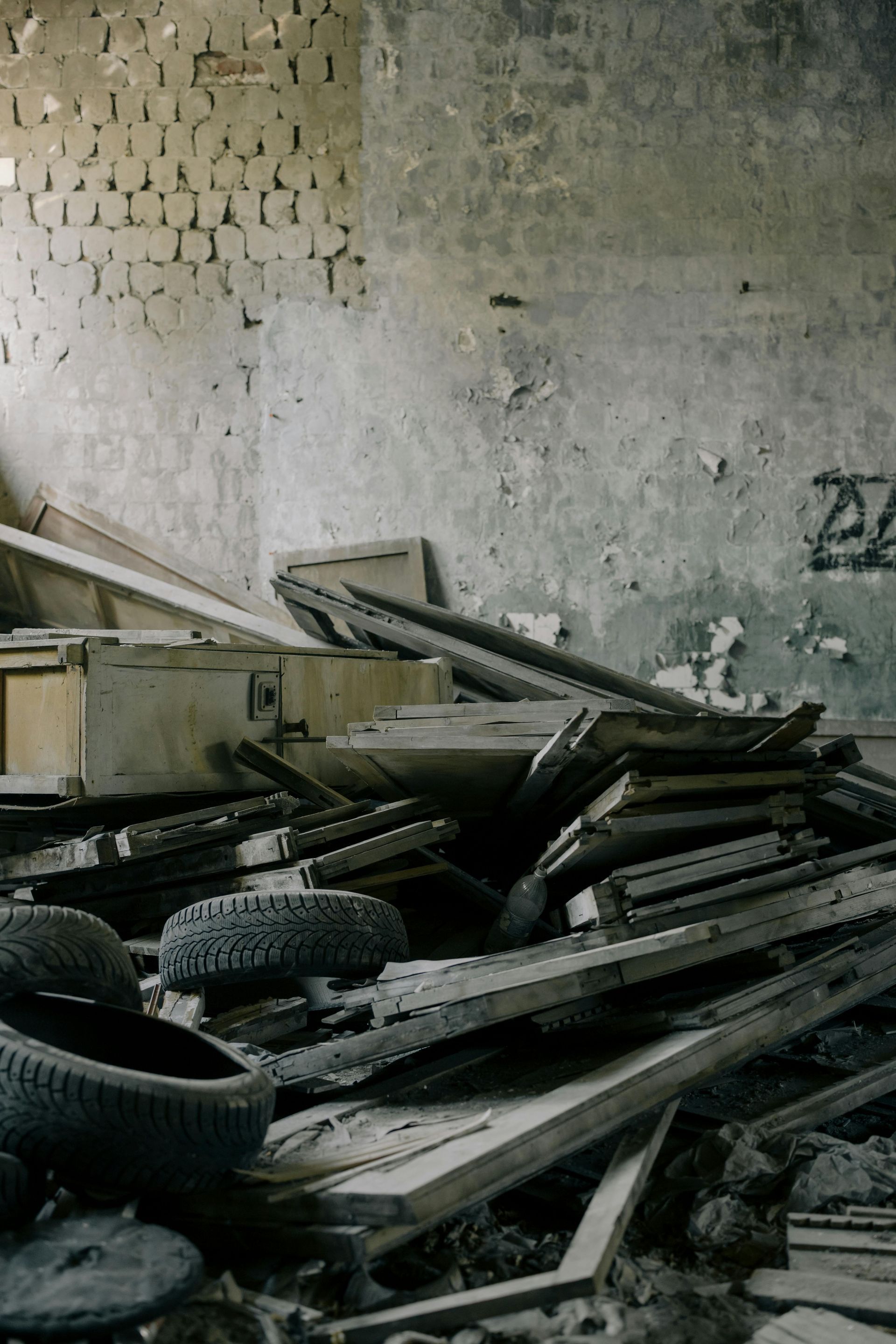Pile of debris in a decaying interior. Includes tires, wood, and weathered walls with graffiti.