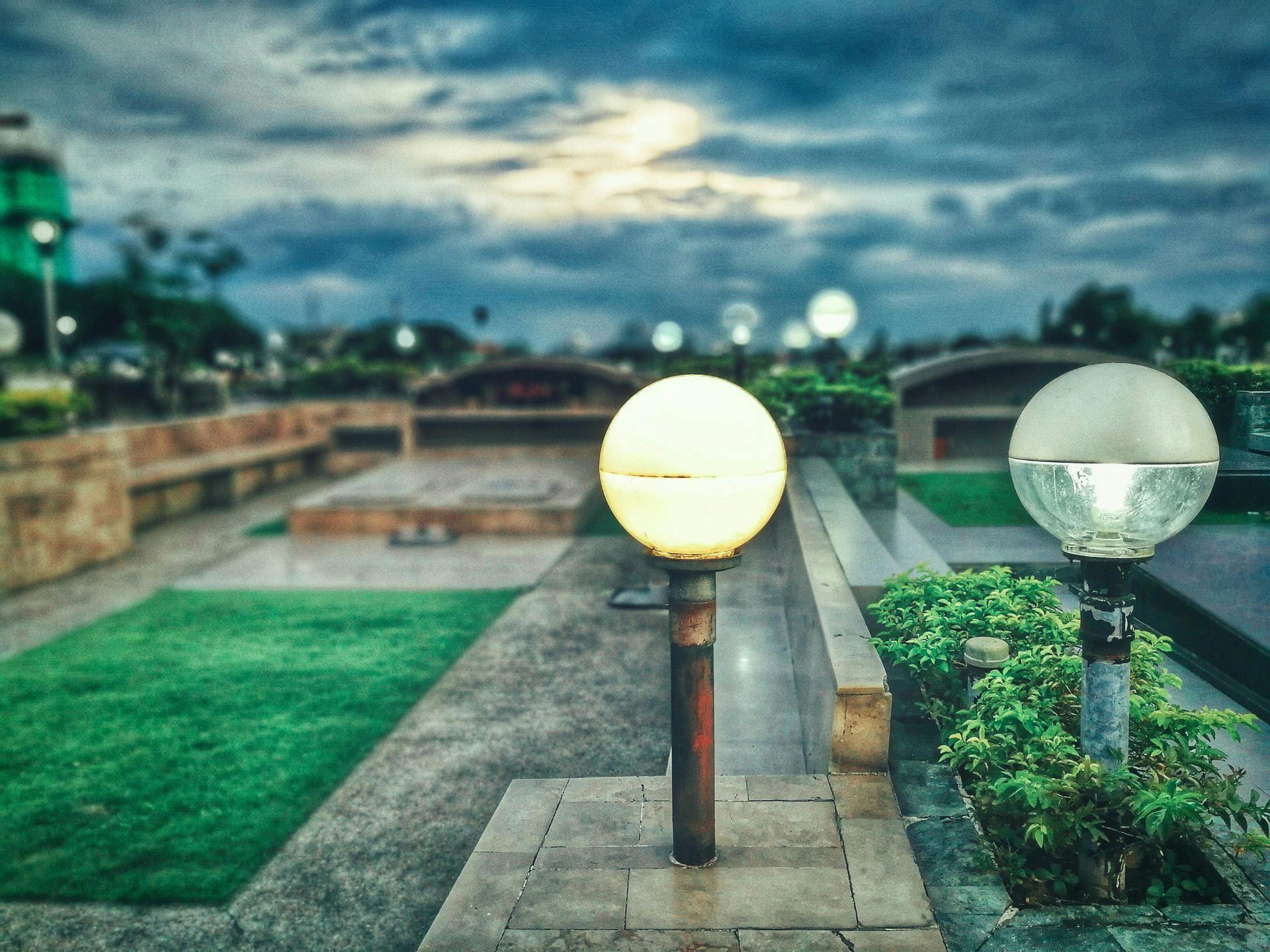 Outdoor scene with glowing spherical lights, a pathway, greenery, and a cloudy sky.