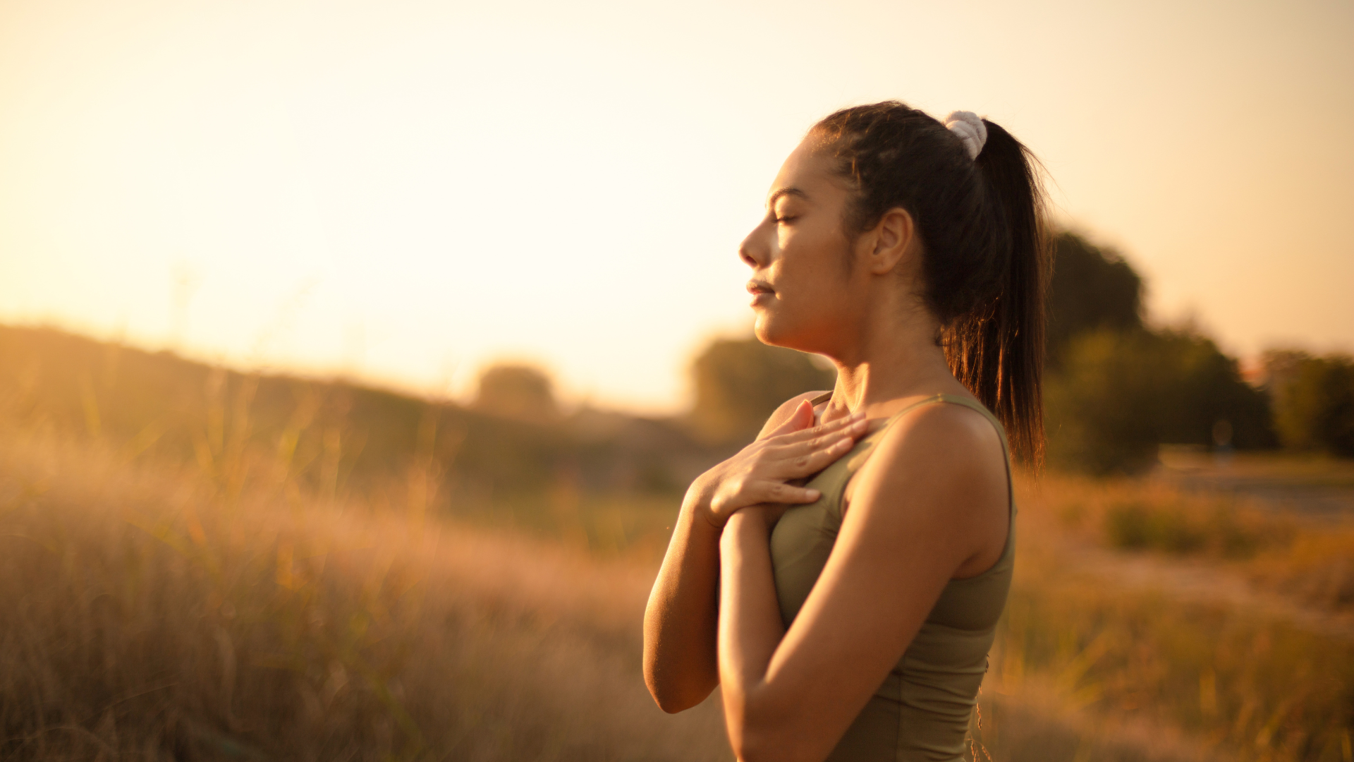 Woman with eyes closed, hands on chest, outdoors in golden sunlight.