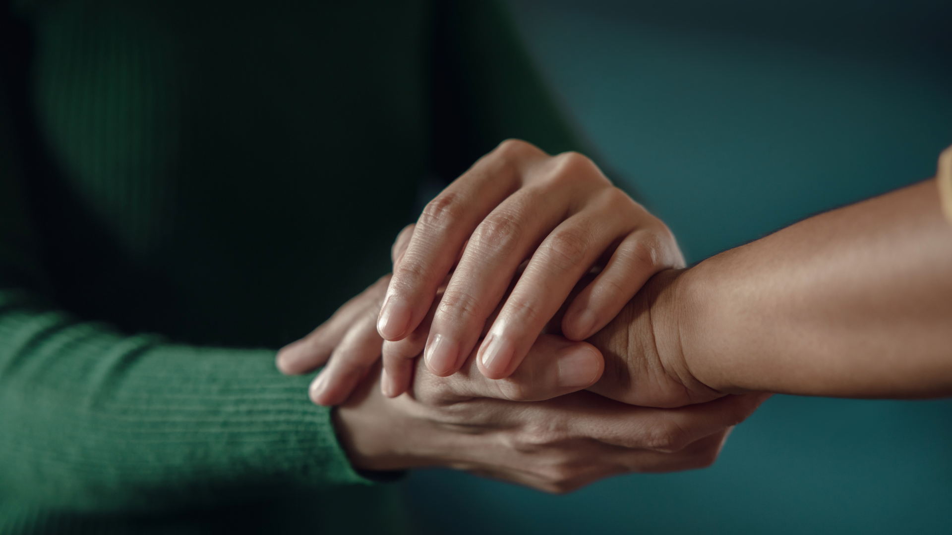 Hands clasped together, one hand gently resting on another, offering comfort and support.
