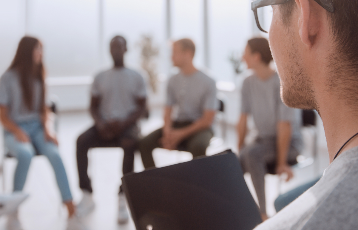 A person in glasses looking at a therapy group; several individuals seated in a circle.