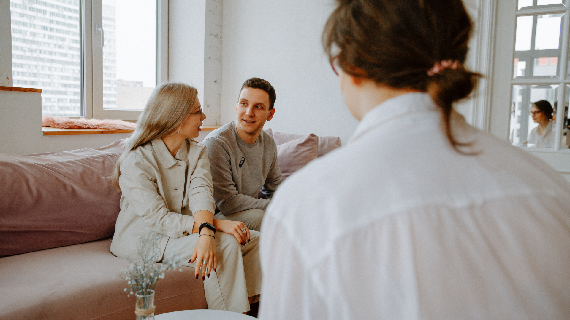 Couple on a pink sofa talking to a person in a white shirt, likely in therapy.