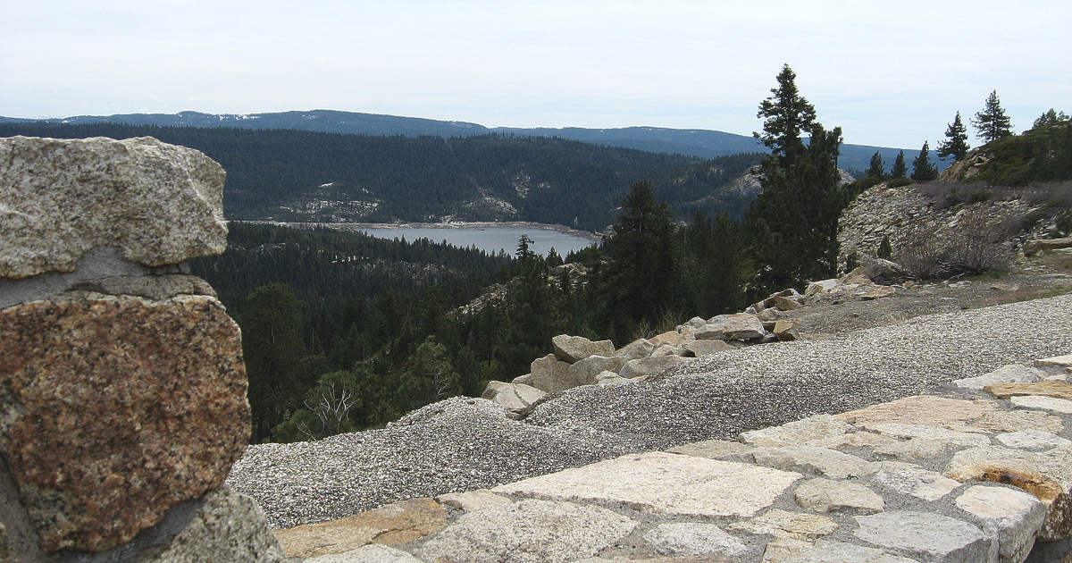 Stone wall in foreground with view of lake and forest on a hazy day.