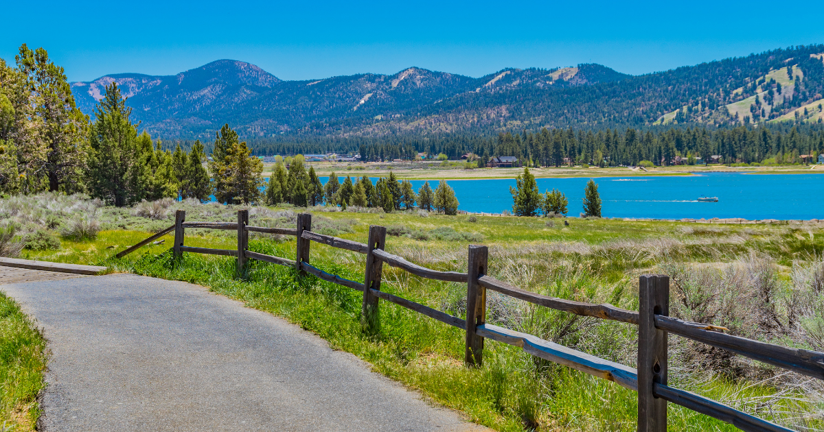 View from Alpine Pedal Path with a wooden fence leading to a lake with mountains in the background  along the northern shore in Big Bear Lake