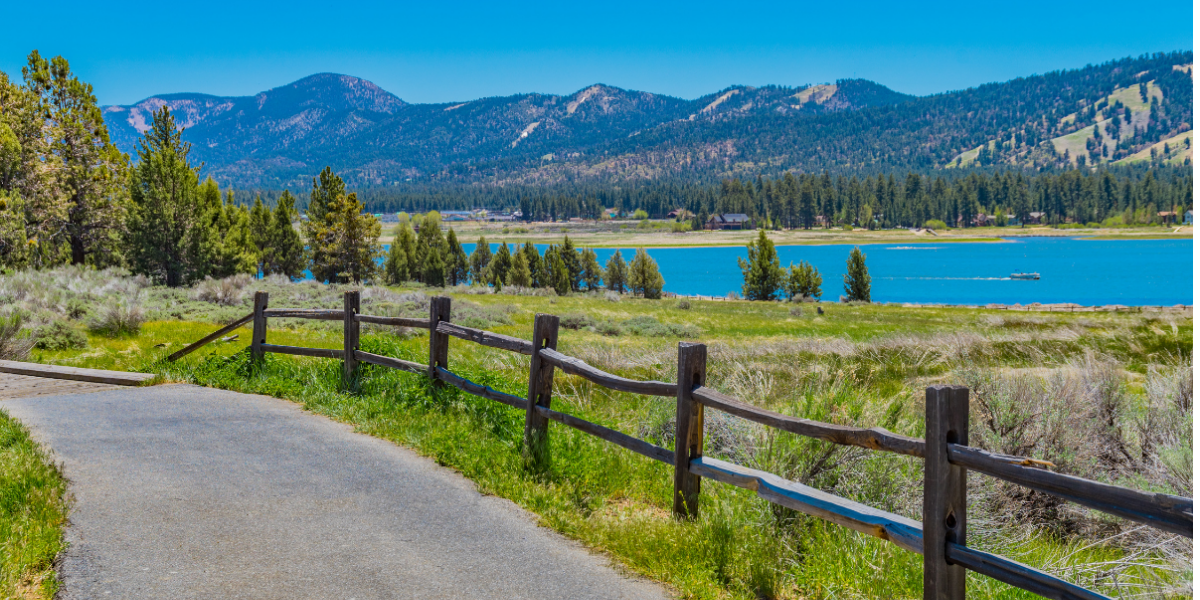 Paved Alpine Pedal Path and wooden fence along Big Bear Lake with mountains in the background under 