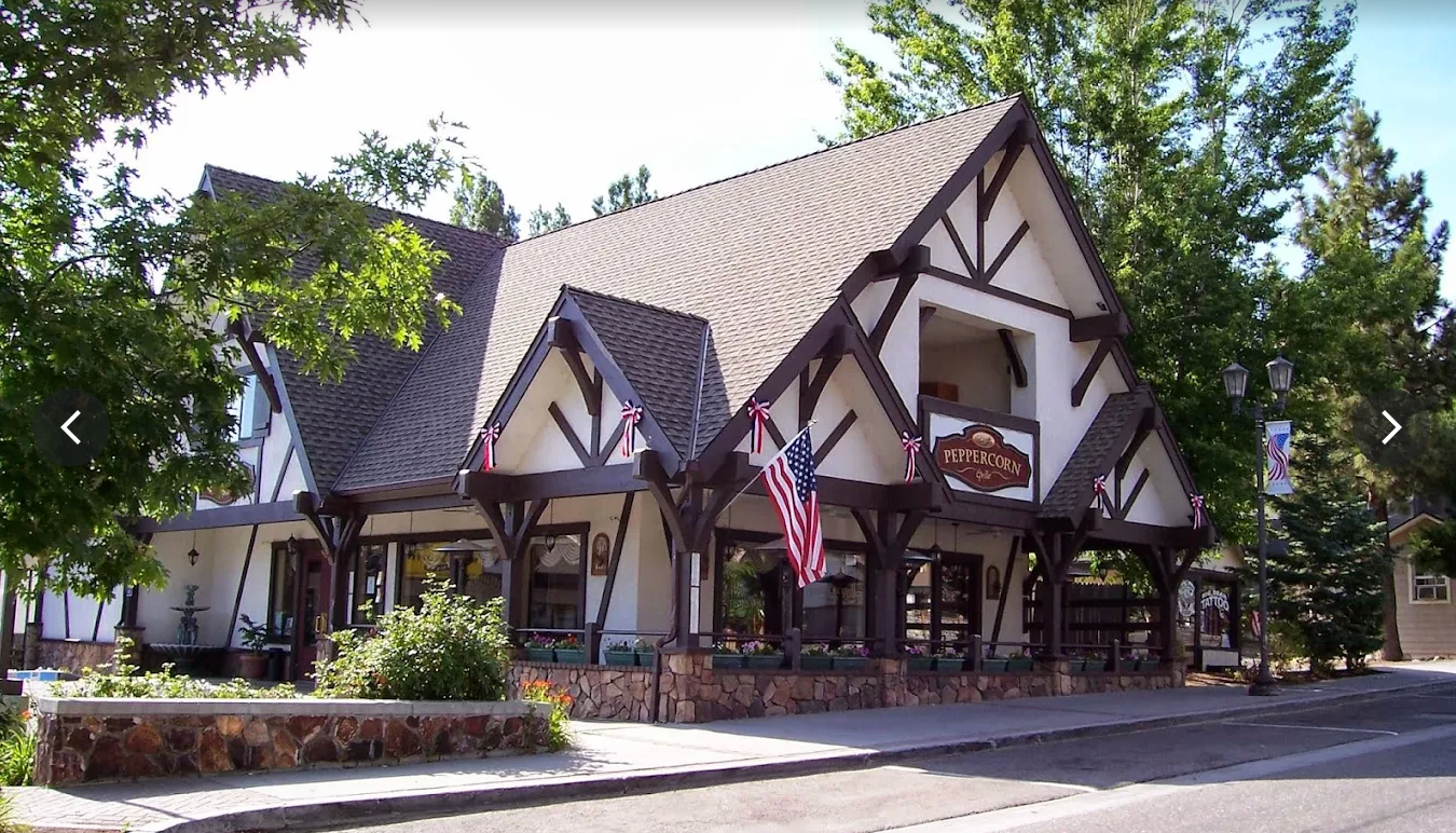Exterior of a The Peppercorn Grille, white and brown Tudor style facade, a porch, and a U.S. flag. 