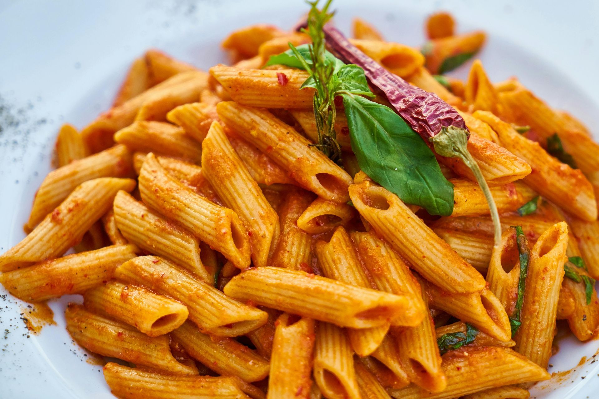 Penne pasta in a red sauce, garnished with fresh basil and a red pepper, served in a white bowl.