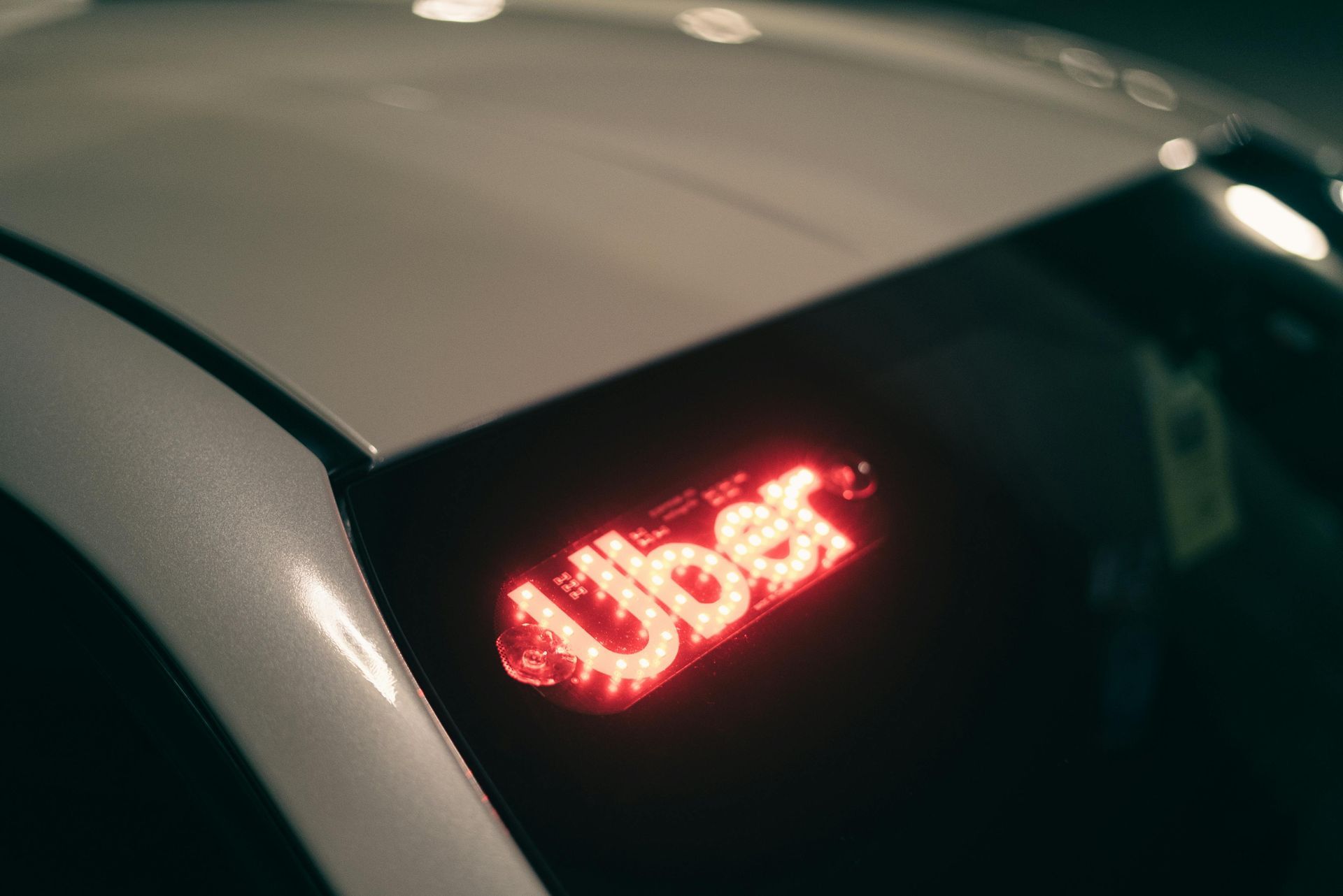 A bright red illuminated Uber sign is displayed on the lower corner of a car windshield at night.