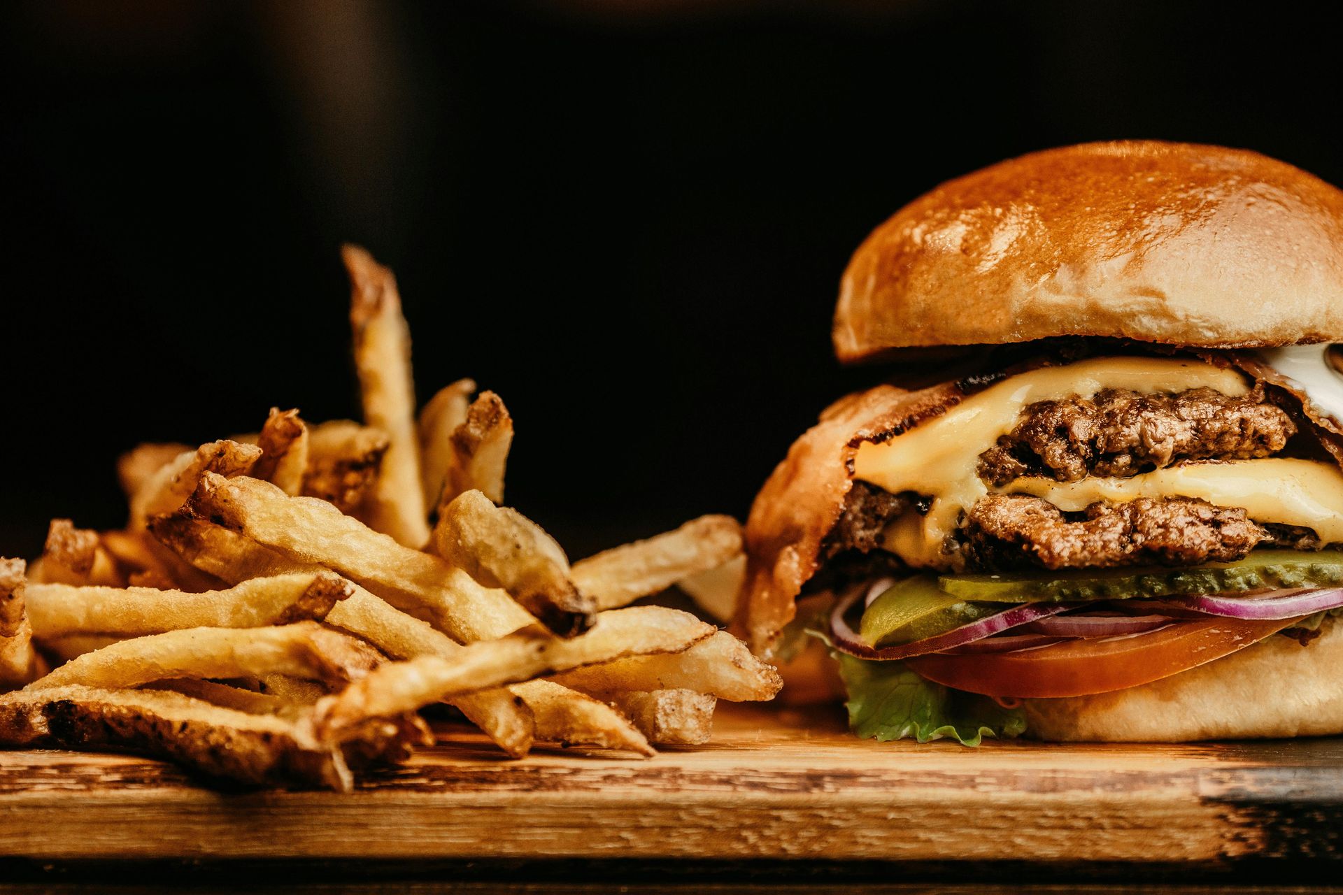 Burger with fries on a wooden board. The burger has two patties, cheese, and toppings. Fries are golden brown.