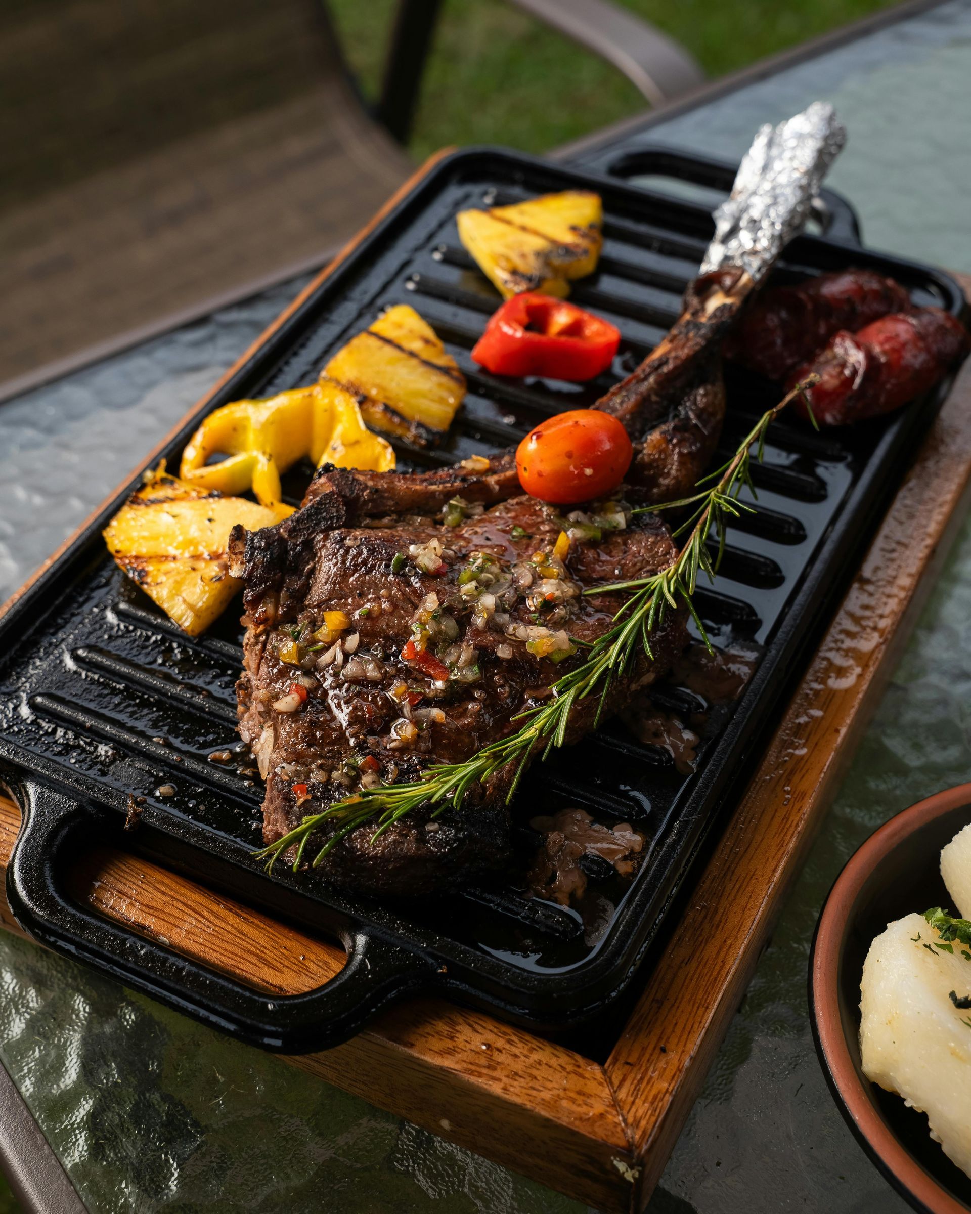 Grilled steak with vegetables and sausage on a cast iron griddle, set on a wooden board.