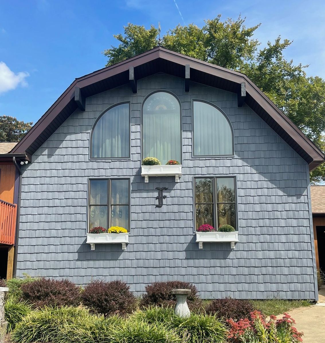 A gray house with a brown roof and arched windows with garden in front