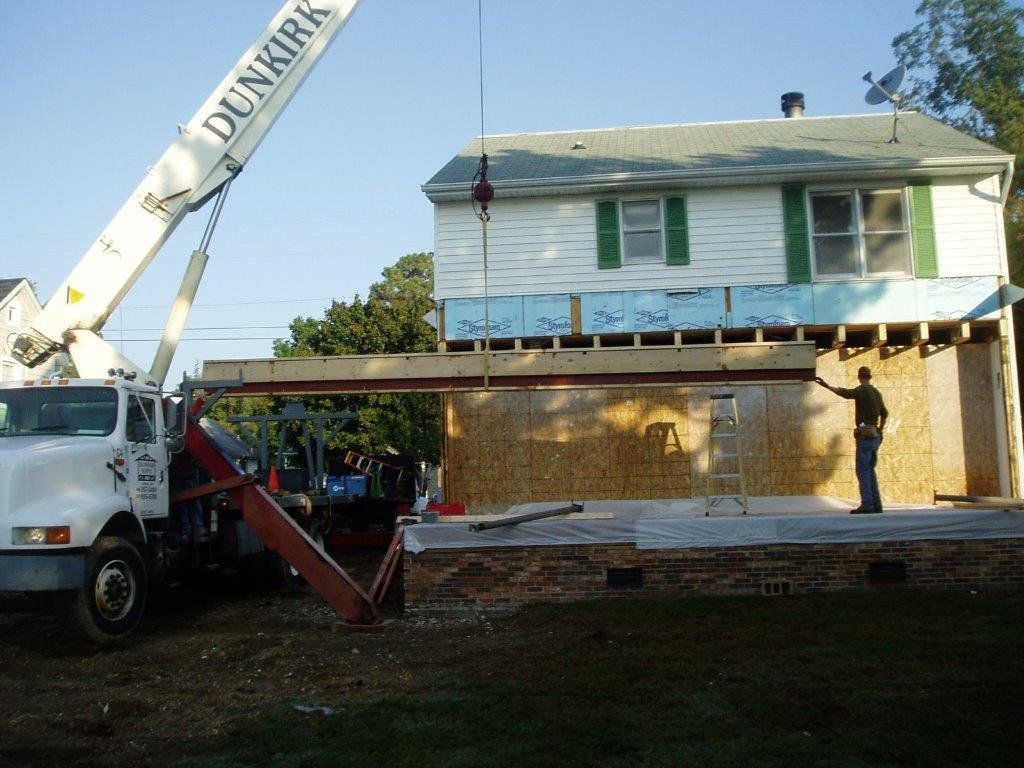 A crane is lifting a piece of wood onto a house