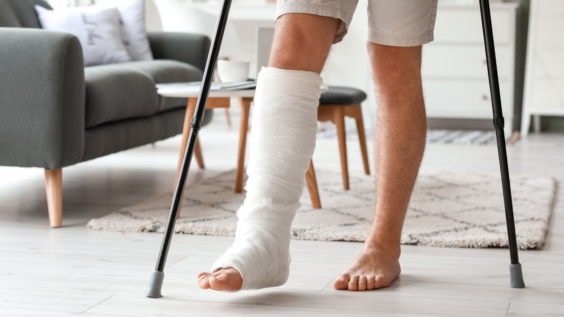A person with a cast on their leg is standing on crutches in a living room.