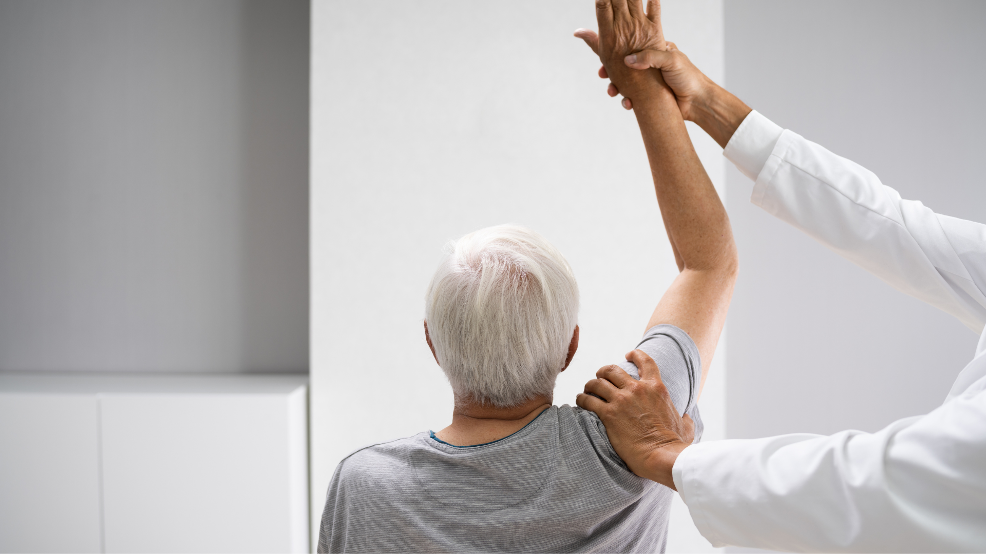 An elderly man is being examined by a doctor who is stretching his arm.