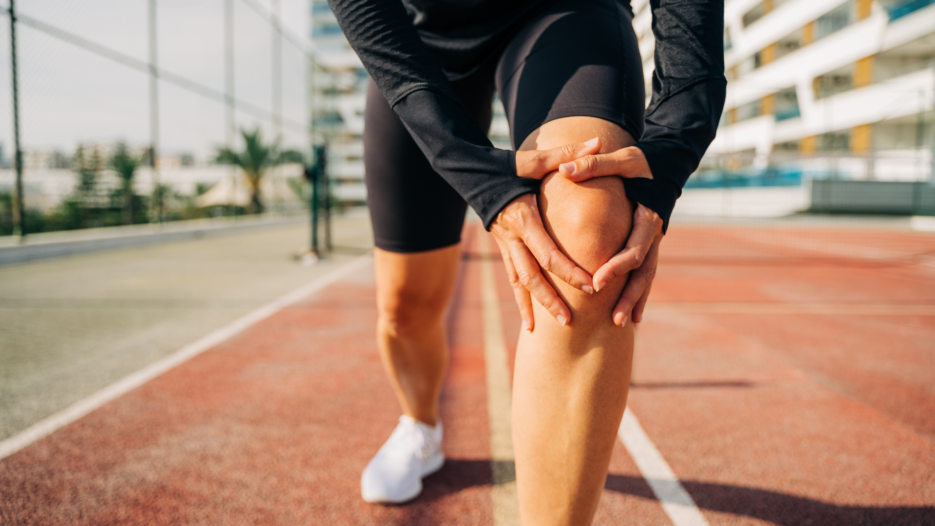 A woman is holding her knee in pain on a track.