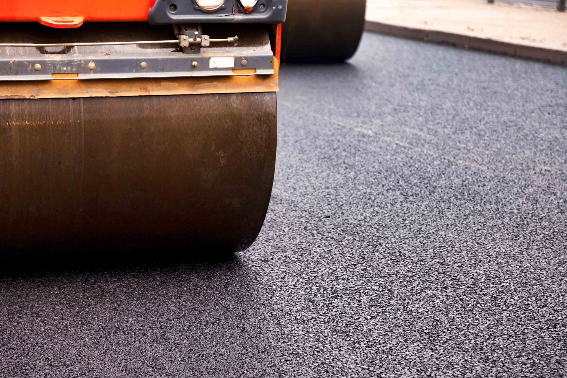 A heavy construction roller on a freshly laid, textured asphalt surface.