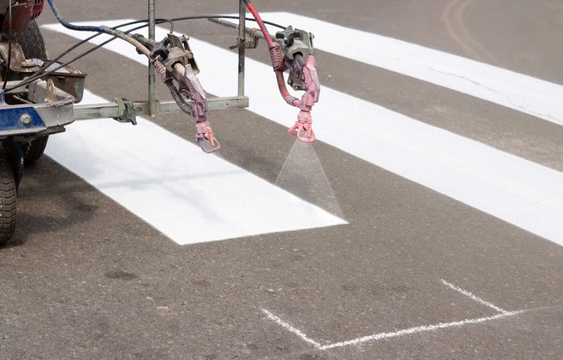 A mechanical sprayer paints white rectangular stripes on asphalt to create a pedestrian crosswalk.
