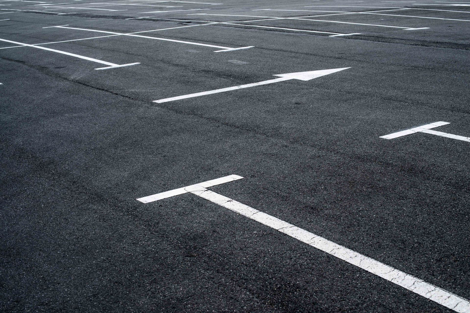A series of white parking space lines painted on a dark asphalt surface, with an arrow indicating a traffic direction.