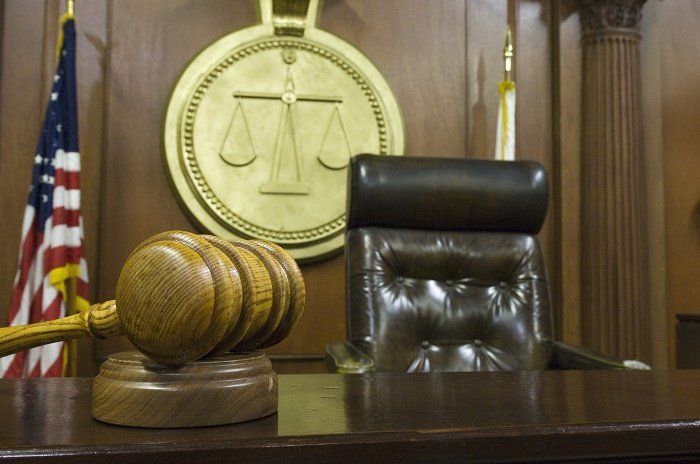 Judge's chair in the courtroom, with gavel on desk and scales of justice in background.