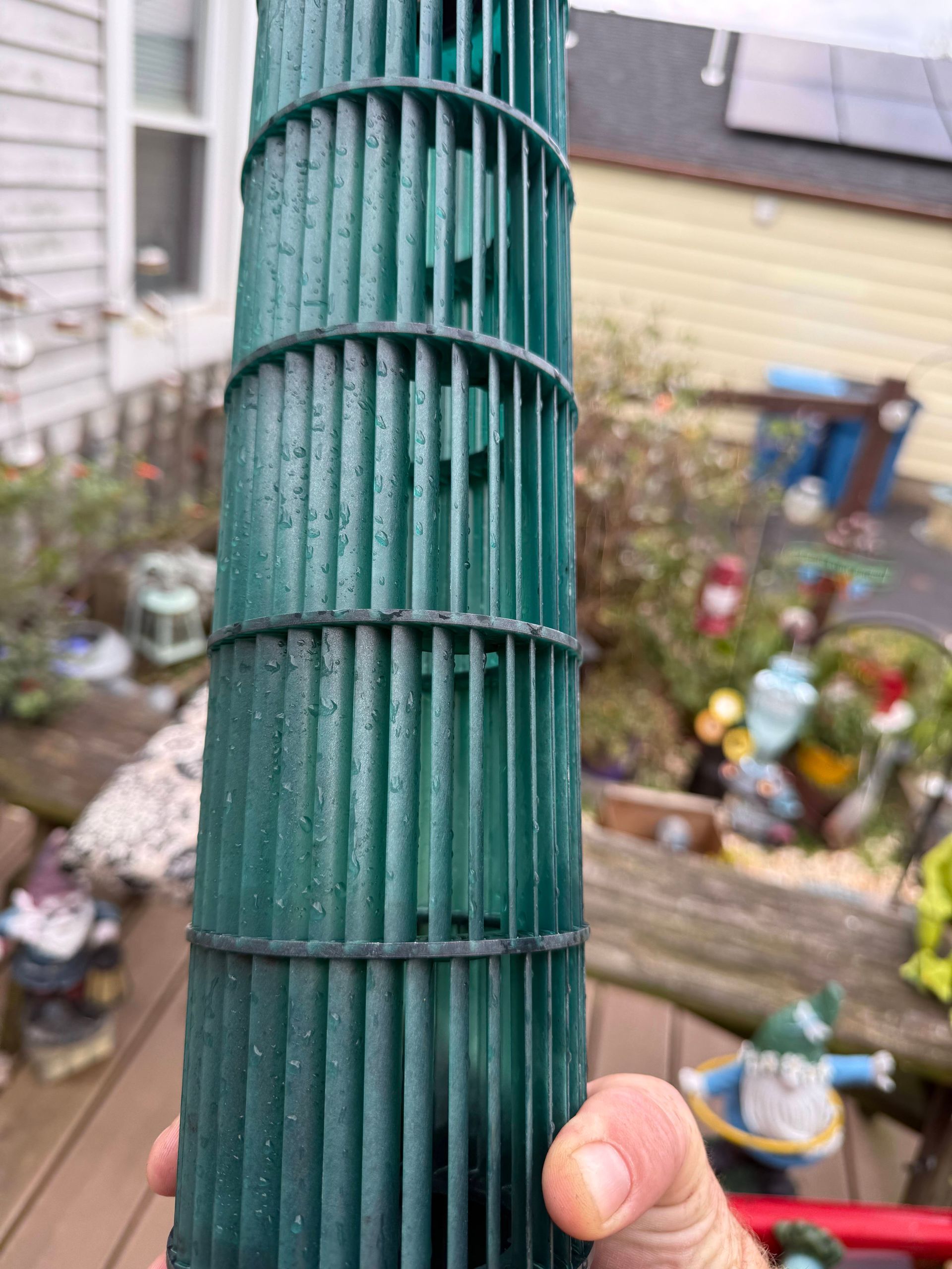A hand holds a tall, cylindrical green blower fan wheel from a ductless air conditioning unit outdoors.