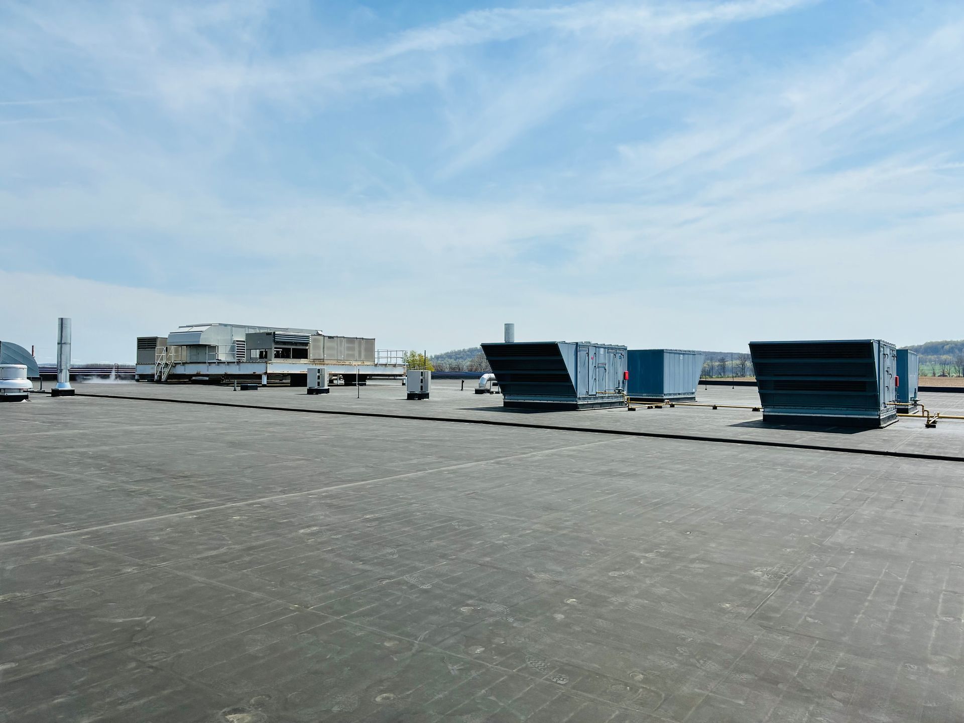 A flat, dark commercial rooftop with large rectangular HVAC units under a clear blue sky.