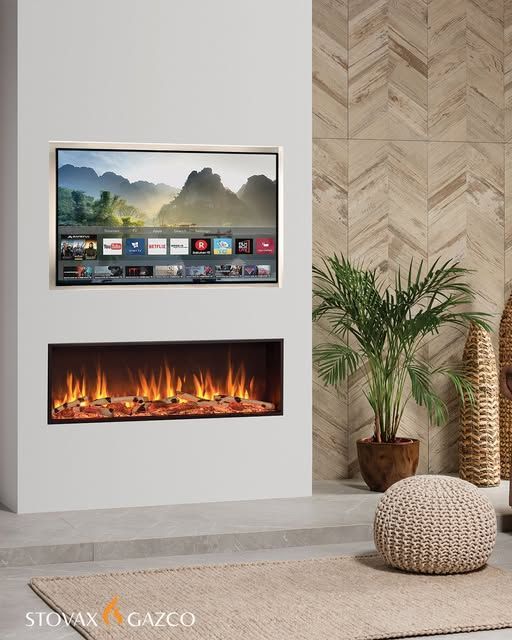 Modern fireplace with a TV above, set in a recessed white wall, with a plant, and beige accents.