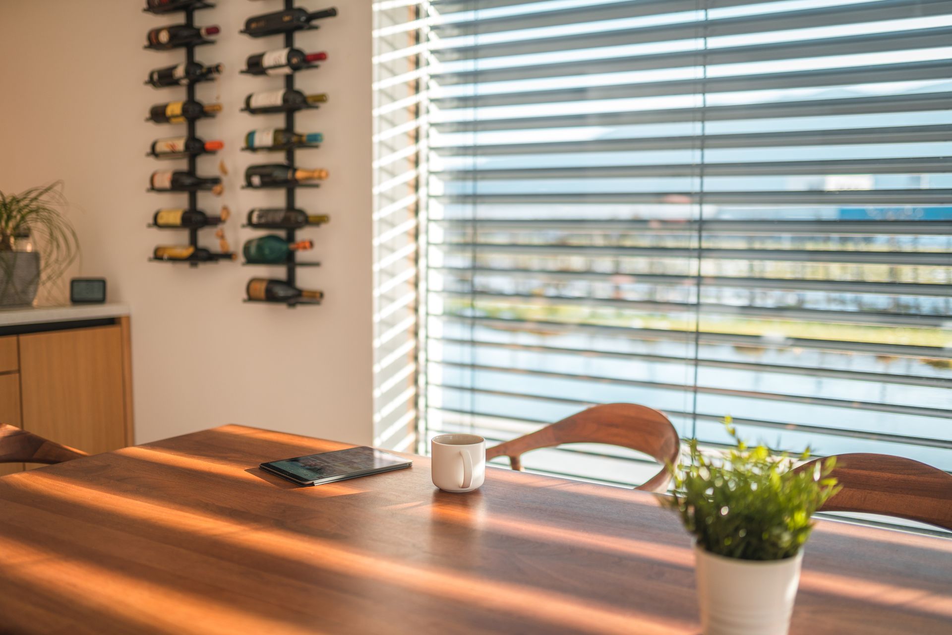 A dining room table with a potted plant on it and a window with blinds.