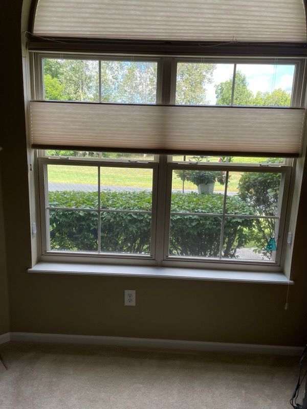 Window with beige shade, looking out to greenery. Beige walls, white windowsill, and tan carpet.