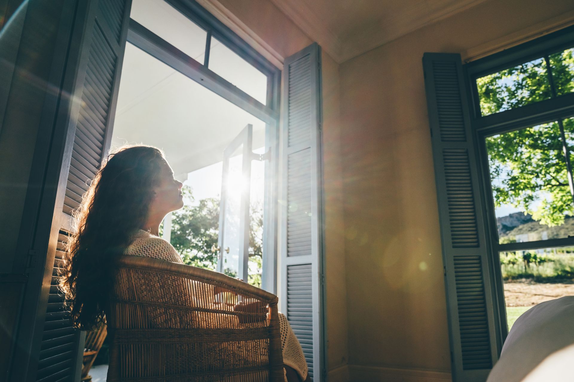 A woman is sitting in a chair looking out of a window.