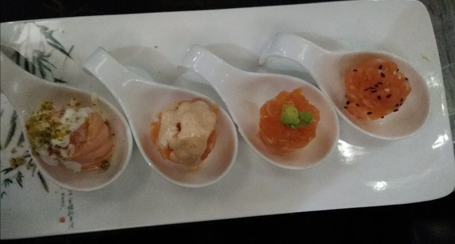 Quattro piccole coppette da dessert su un vassoio rettangolare bianco, ognuna con guarnizioni e colori diversi.