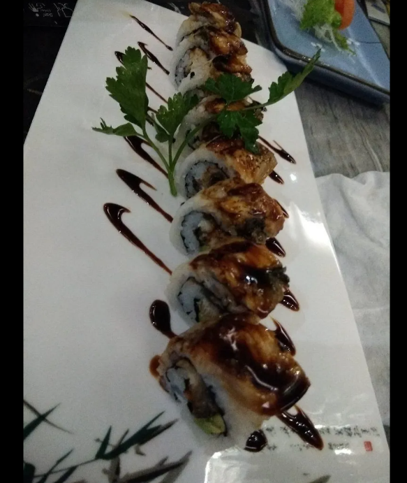 Rotoli di sushi conditi con salsa scura e guarniti con prezzemolo, serviti su un piatto rettangolare bianco.