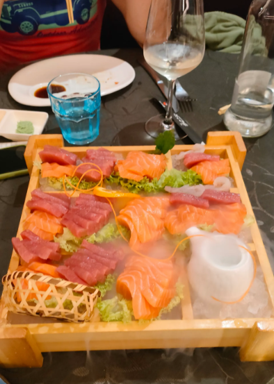 Piatto di sushi su un vassoio di legno con fette di salmone e tonno su un tavolo di ristorante.