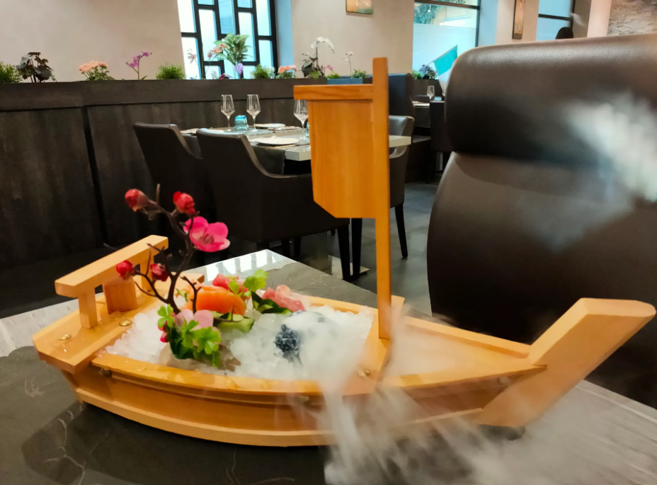 Piatto decorativo a forma di barca per sushi su un tavolo di un ristorante, con fiori ed effetto fumo creato con ghiaccio secco.