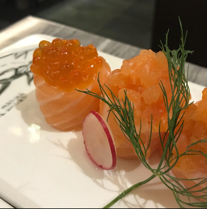 Sashimi di salmone con uova di pesce arancioni, guarnito con aneto e ravanello su un piatto bianco.