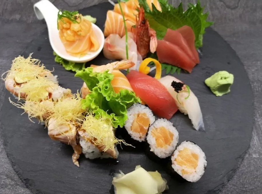 Piatto di sushi con assortimento di sashimi, nigiri e roll su un piatto di ardesia nera con wasabi e guarnizioni.
