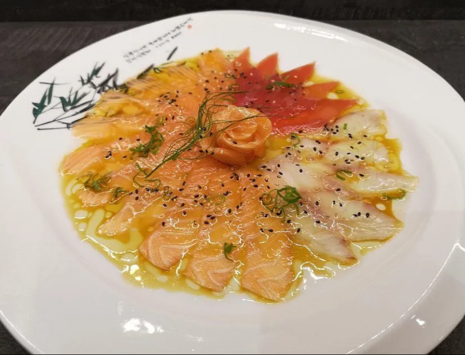 Carpaccio di salmone tagliato finemente con erbe aromatiche, capperi e pepe su un piatto bianco.