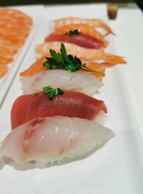 Assortimento di nigiri di sushi su un vassoio bianco, tra cui salmone, tonno e pesce bianco con guarnizione.